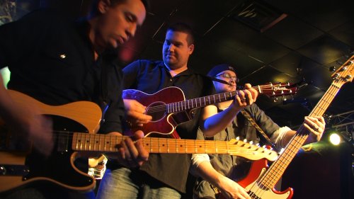 Three guitar players onstage posing together while playing